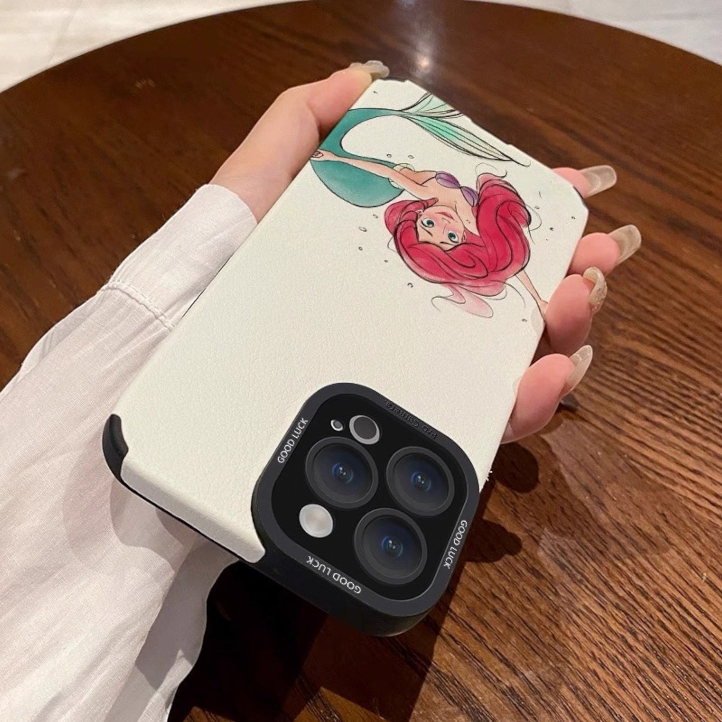 Phone case with a mermaid design held by a hand on a wooden surface