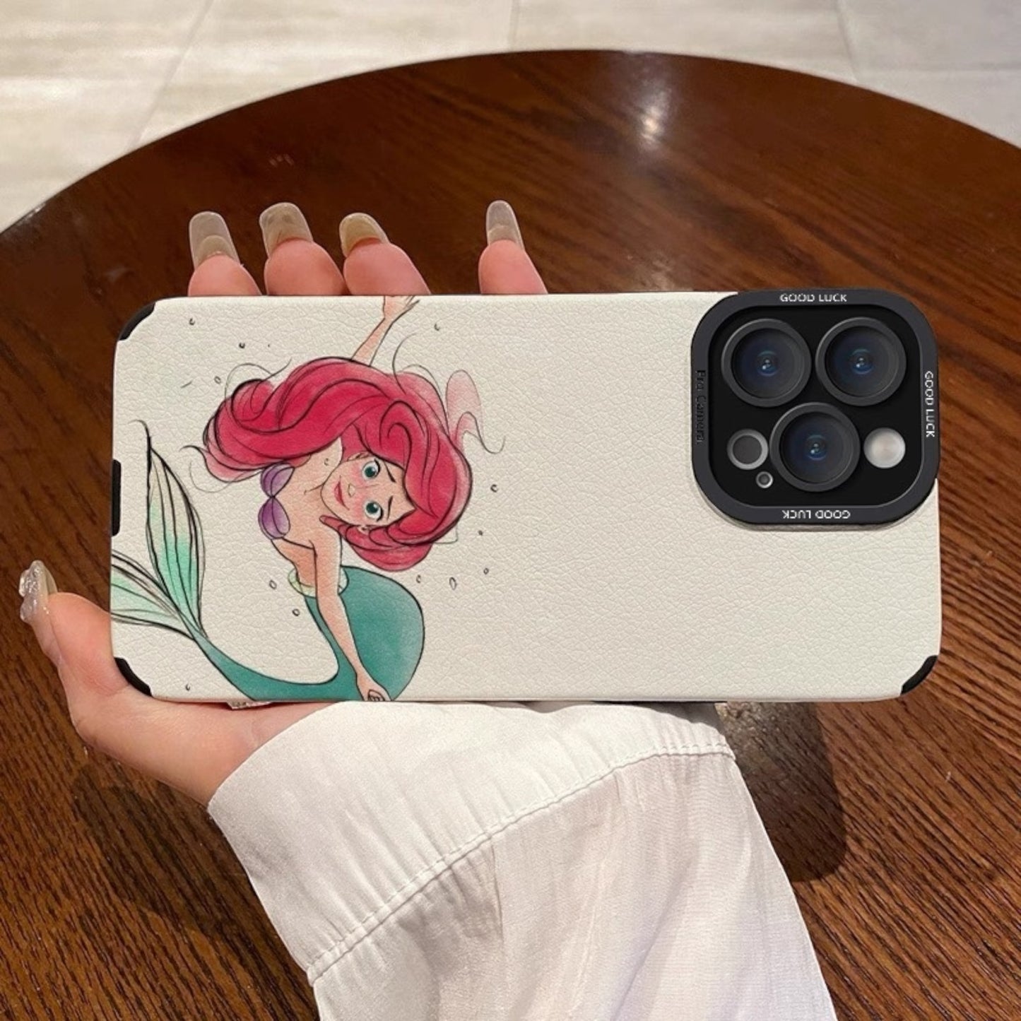 Phone case with a cartoon mermaid design held by a person on a wooden surface