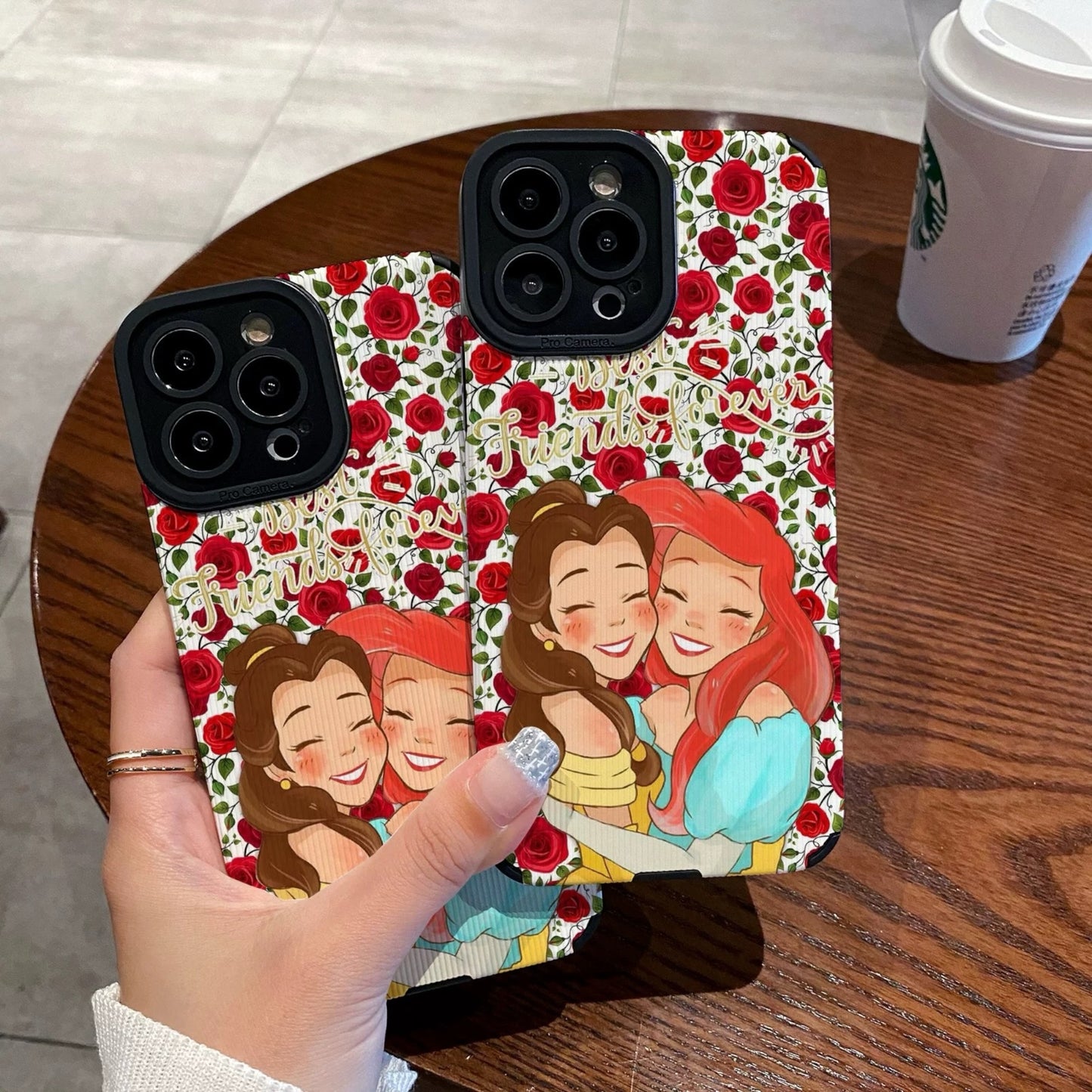 iPhone case with cartoon characters Princess Ariel and Belle on a wooden table with a Starbucks cup.