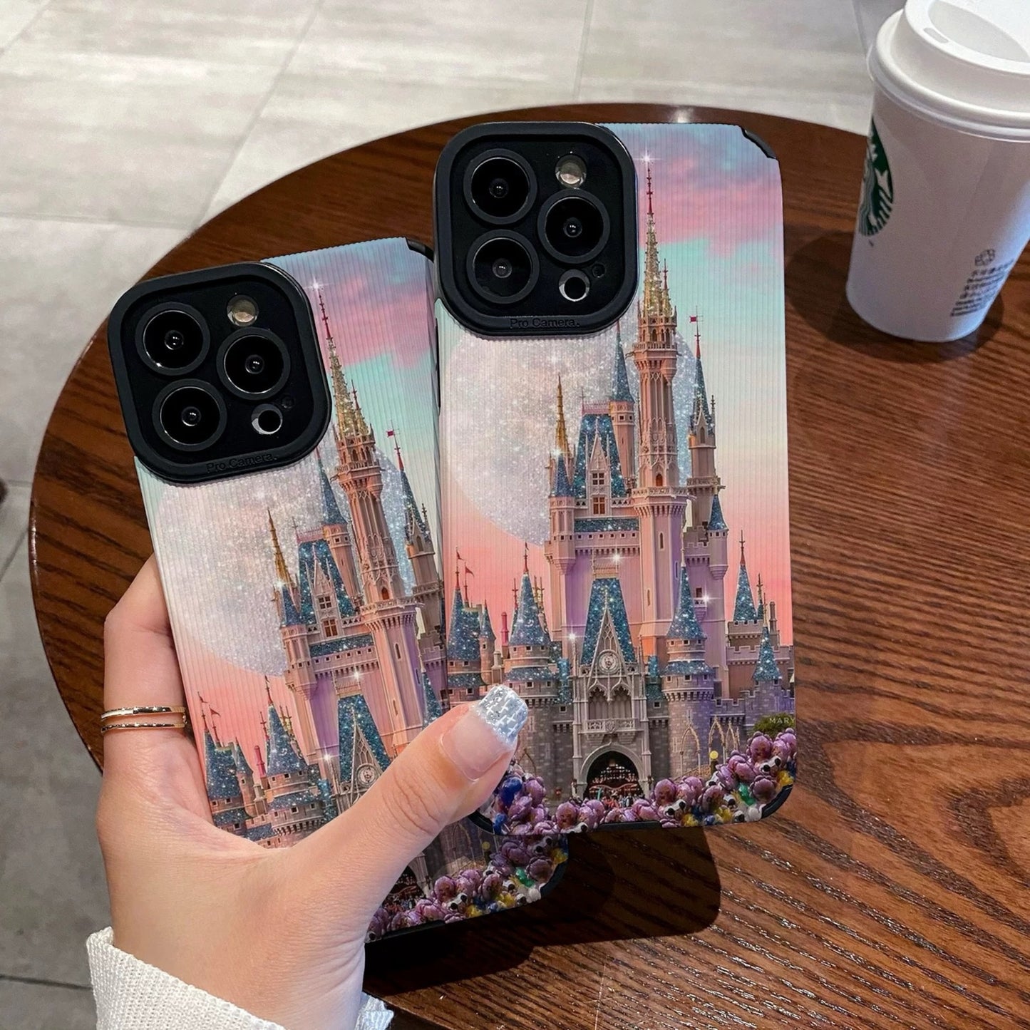 Person holding a iphone with a colorful iphone case featuring a disney theme park castle design, Starbucks cup in the background.