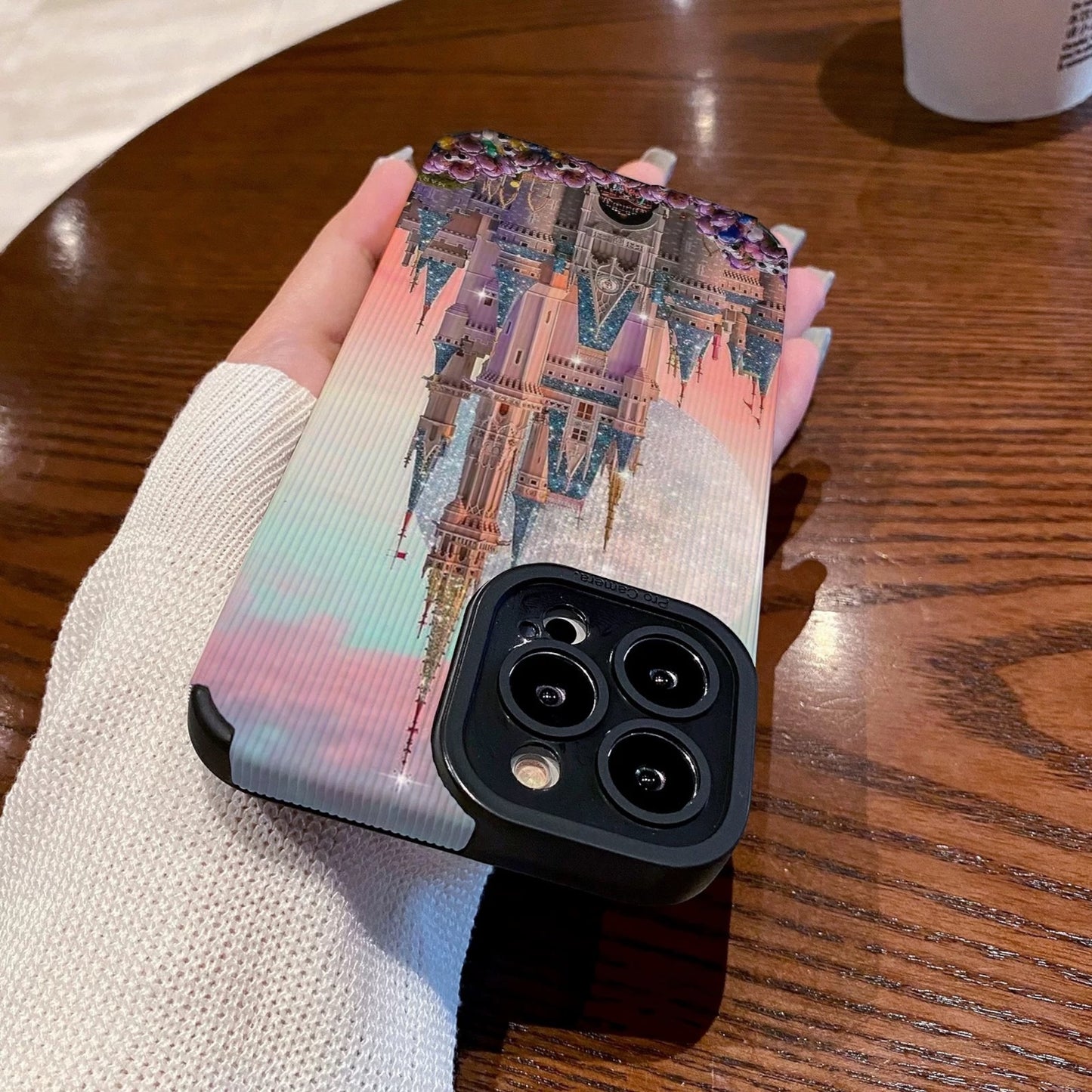 Person holding a iphone with a colorful iphone case featuring a disney theme park castle design, Starbucks cup in the background.