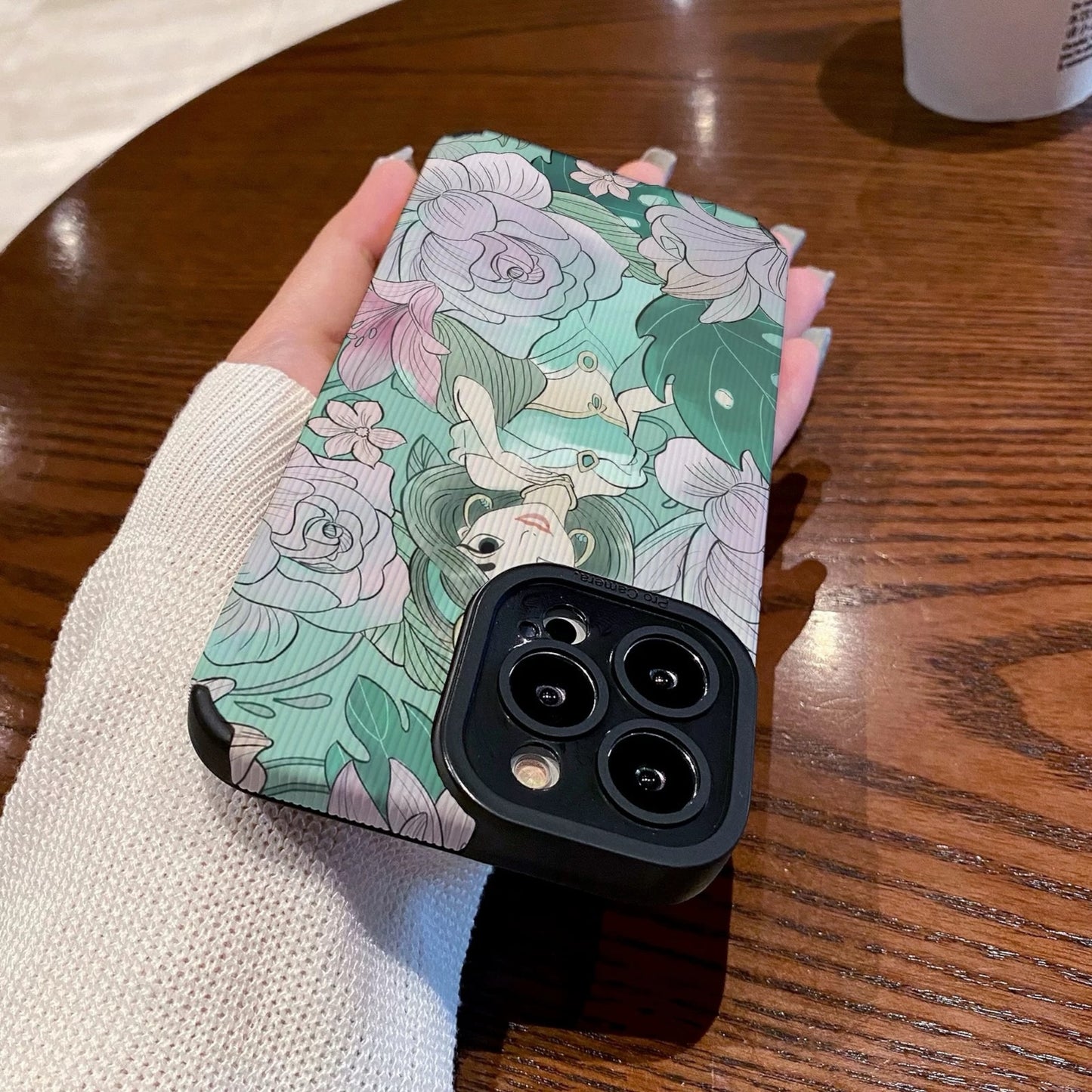 Hand holding a iPhone case with a Jasmine with floral design and character, Starbucks cup in the background.