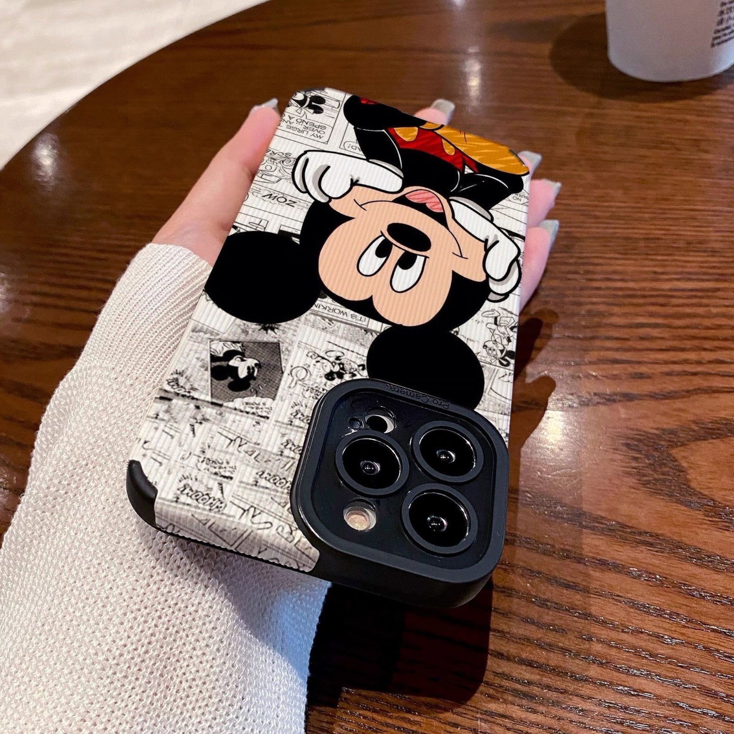 iPhone case with Mickey Mouse design held by a person on a wooden table.