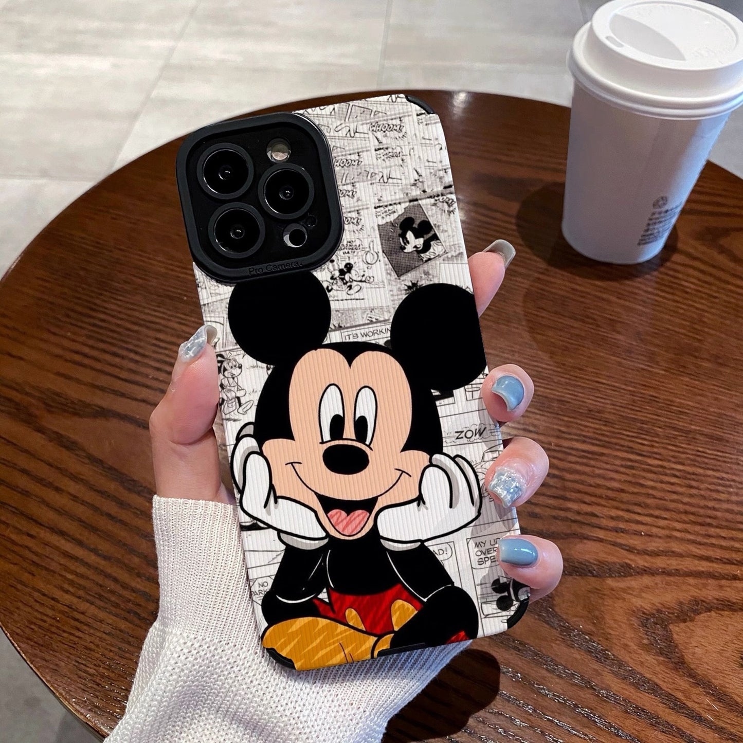 iPhone case with Mickey Mouse design held by a person on a wooden table.