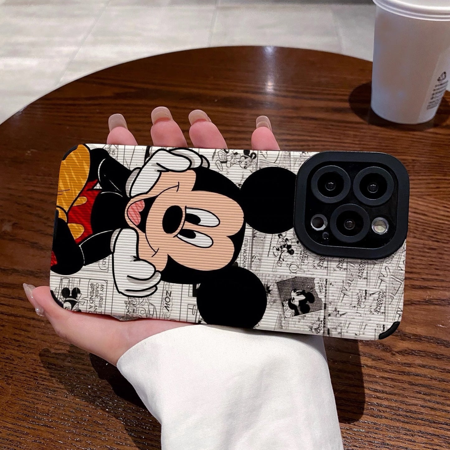 iPhone case with Mickey Mouse design held by a person on a wooden table.