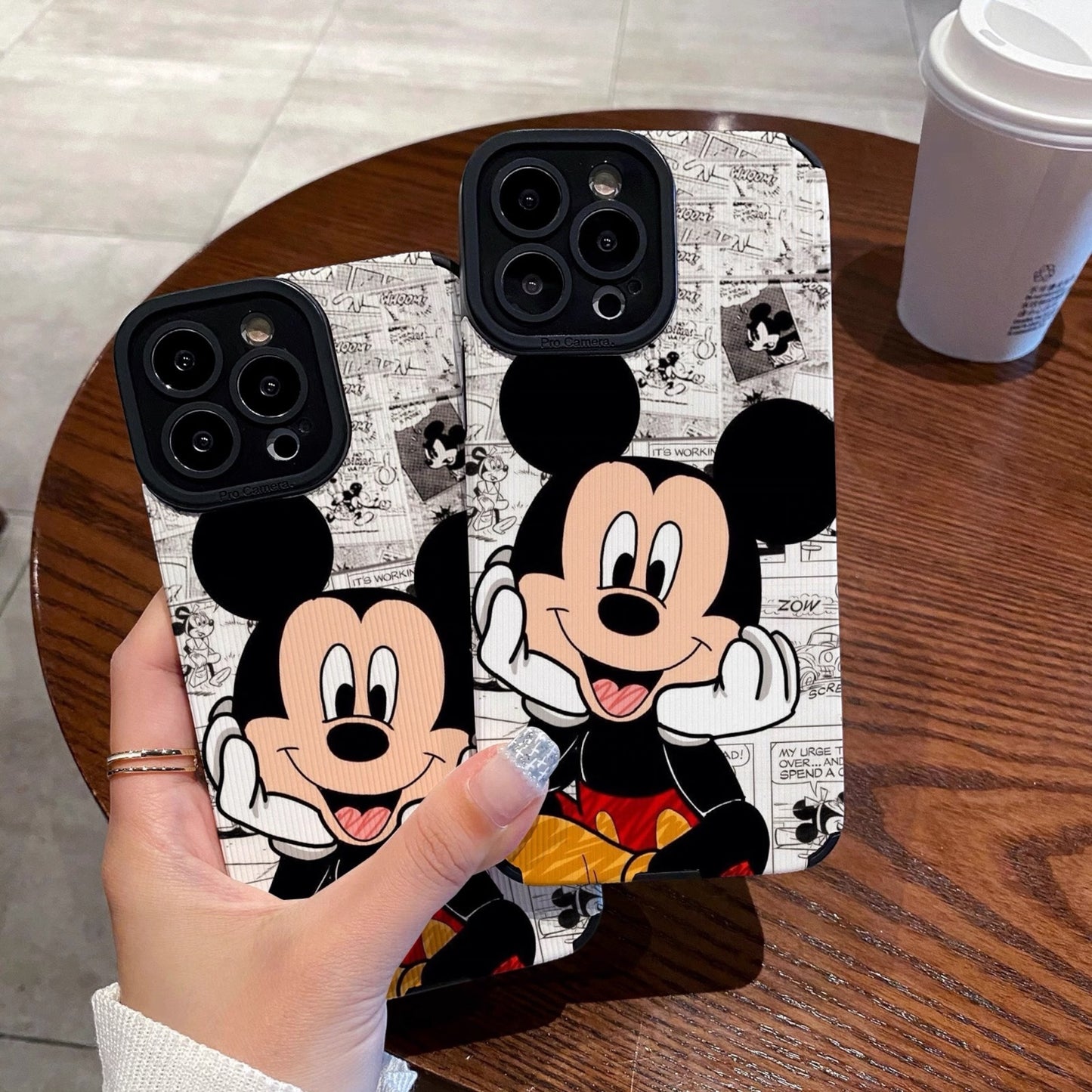iPhone case with Mickey Mouse design held by a person on a wooden table.