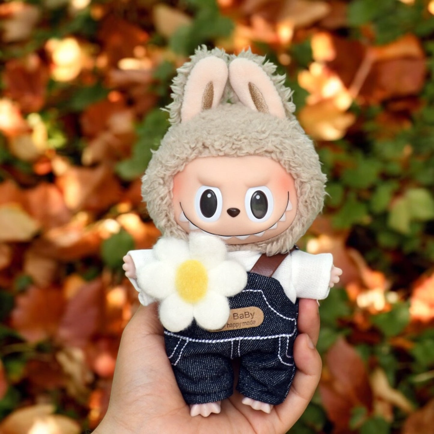 A Labubu Doll wearing a fall in Winter outfits holding by a hand in the forrest