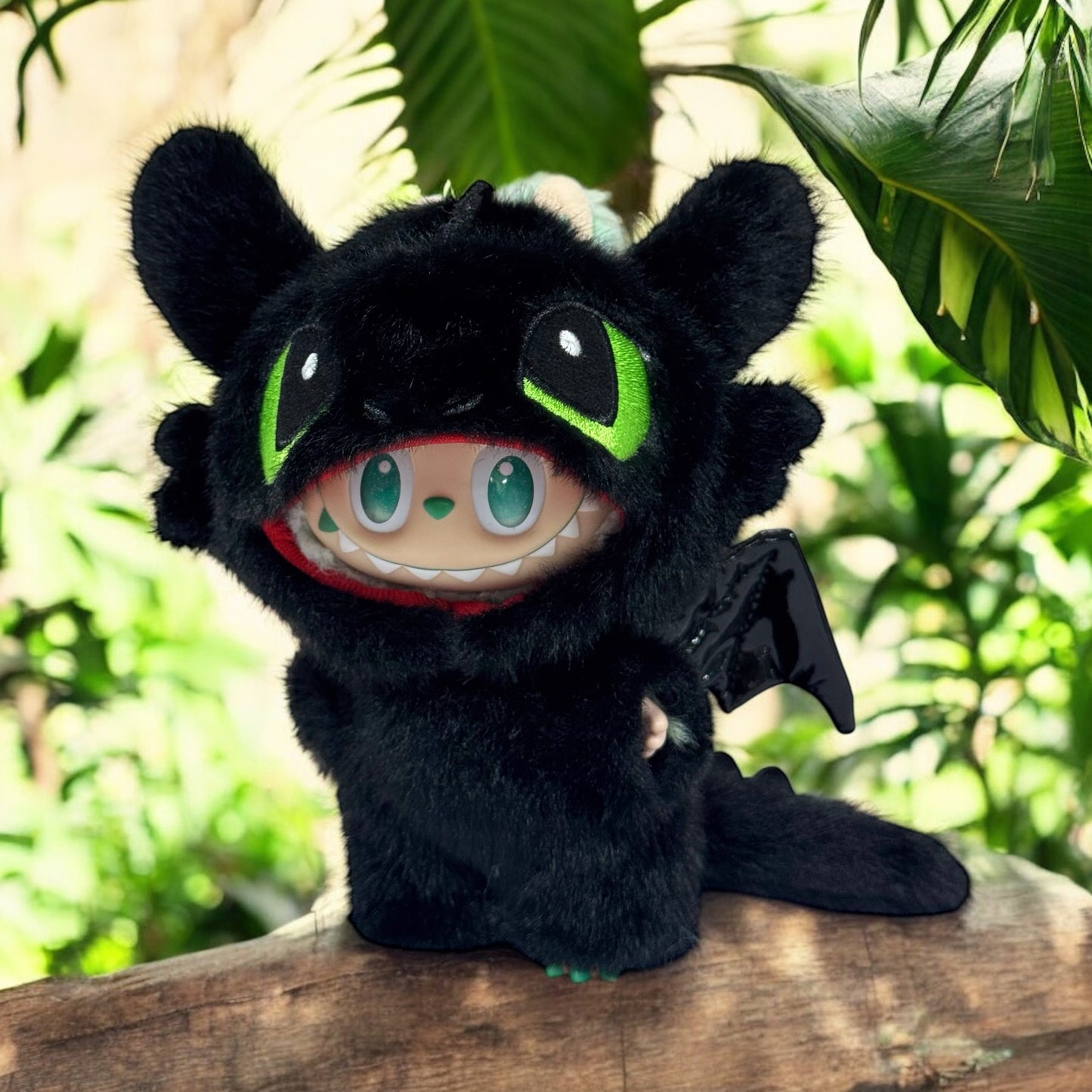 Labubu Plush toy wearing a toothless Costume - a dragon with black fur, green eyes, and red mouth in a forest setting.