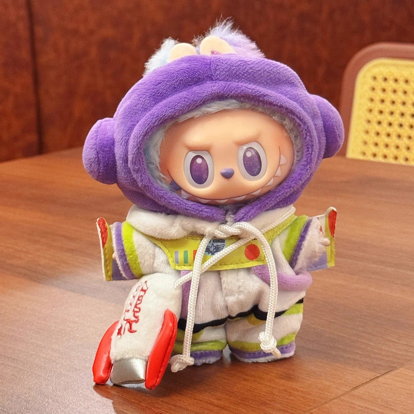 Plush toy buzz lightyear with a purple hood and colorful outfit on a wooden surface
