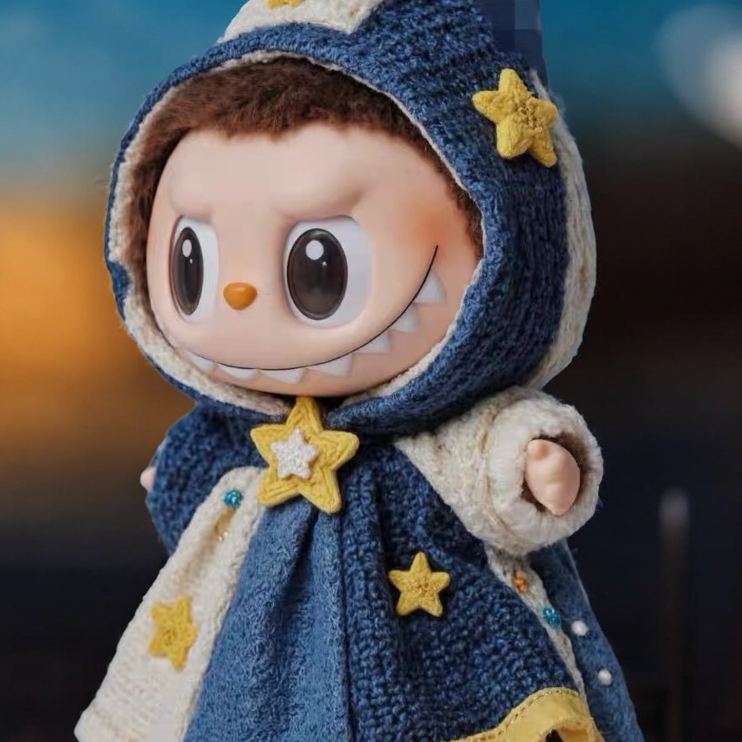 Toy figure Labubu wearing in a blue hooded cloak with star decorations against a Van Gogh painting background