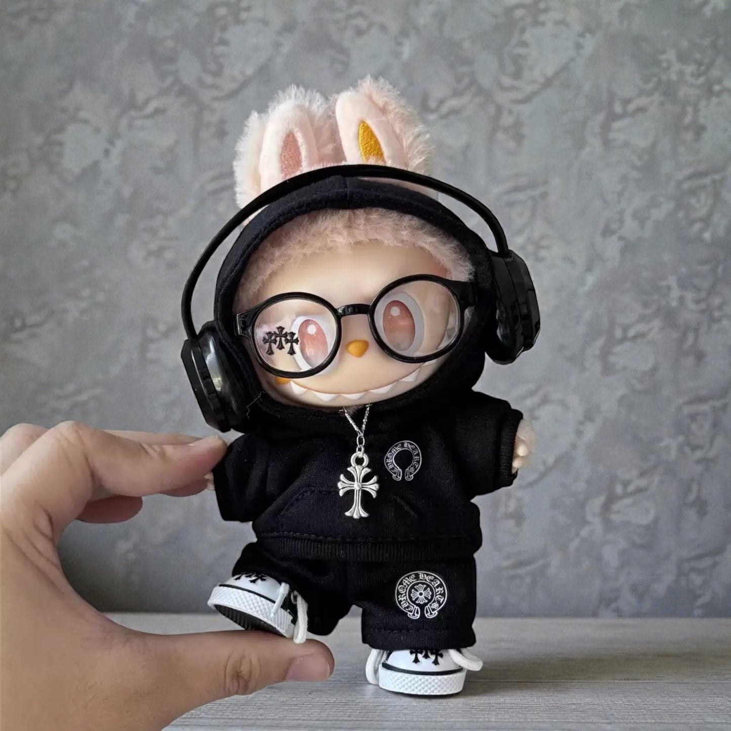 17cm Labubu doll wearing headphones and a black outfit with a hand holding it against a gray background