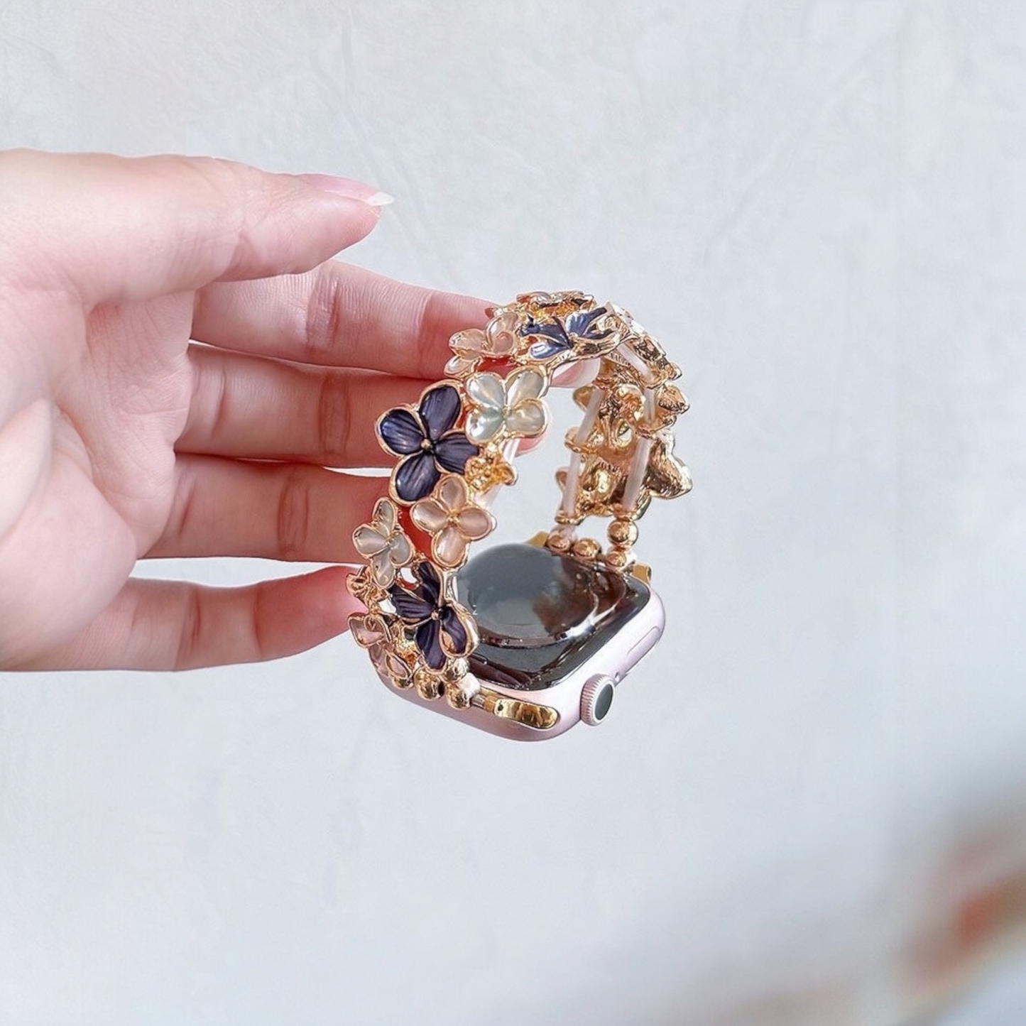 gold-apple-watch-bracelet-purple-enamel-flowers-rhinestones-holding-in-hand