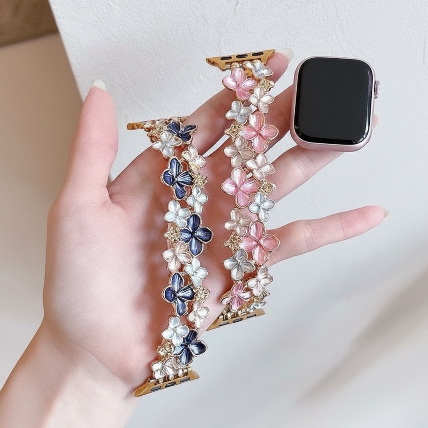 Hand holding a smartwatch with decorative floral band against a neutral background