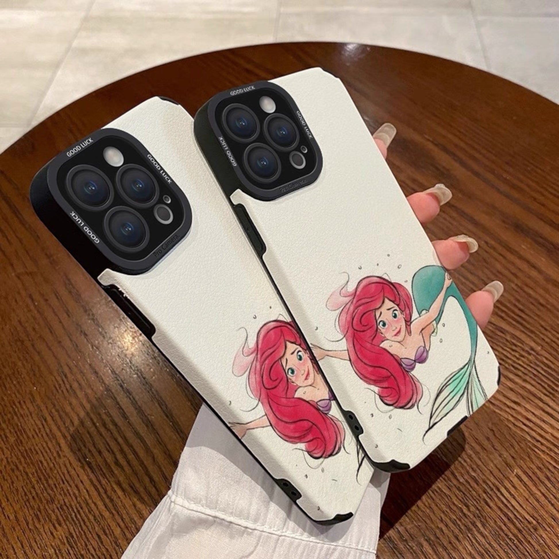 Phone case with mermaid design held by a hand on a wooden surface