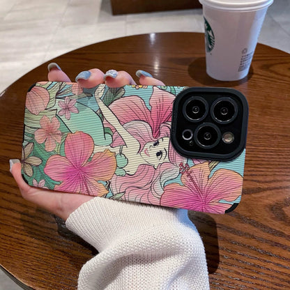 iPhone case with Ariel in  floral design held by a hand on a wooden table with a Starbucks cup in the background.