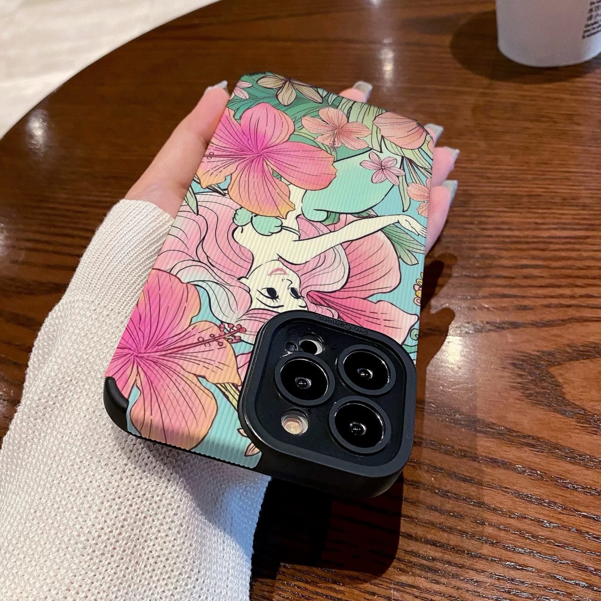 iPhone case with Ariel in  floral and fairy design held by a hand on a wooden surface