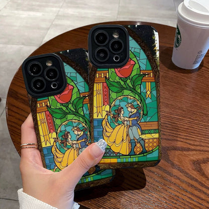 iPhone case with stained glass design with belle and the prince held by a hand on a wooden table with a Starbucks cup.