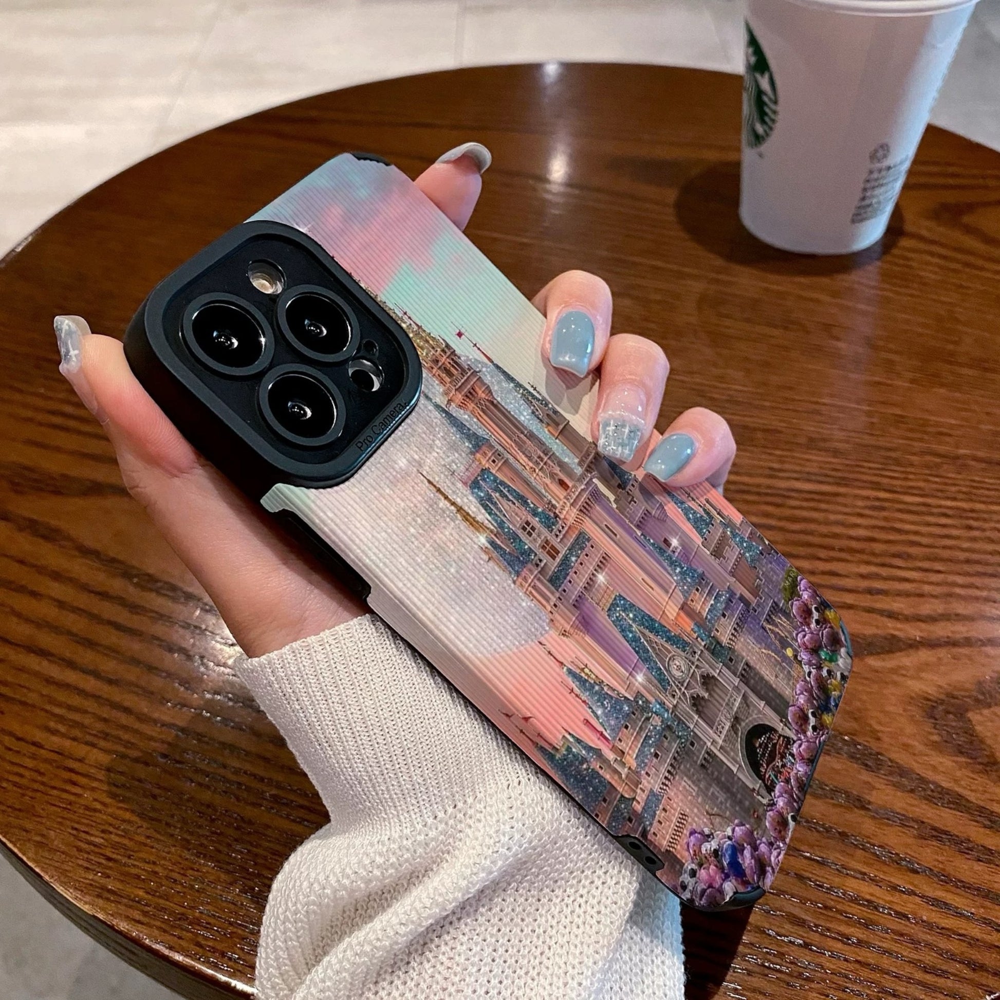 Person holding a iphone with a colorful iphone case featuring a disney theme park castle design, Starbucks cup in the background.
