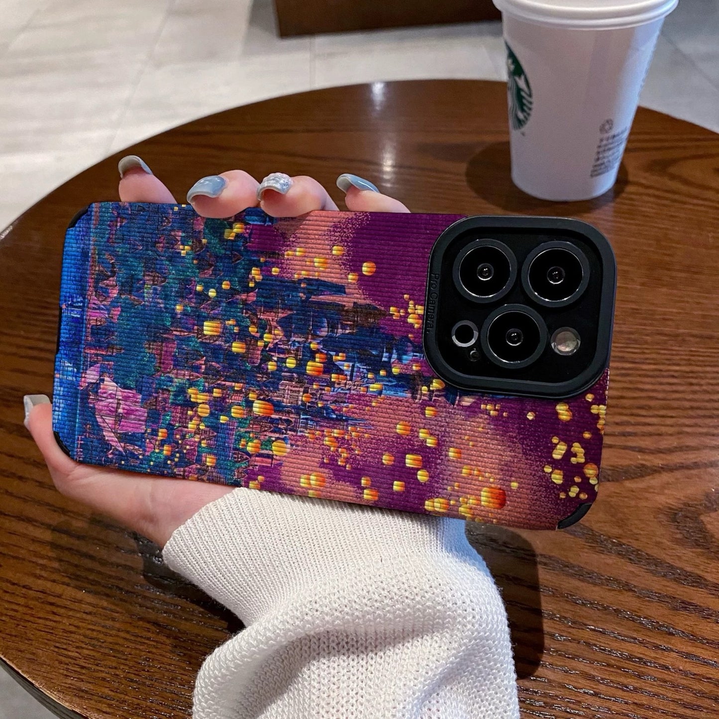 Hand holding a iPhone case with a colorful castle design on a wooden table with a Starbucks cup in the background.