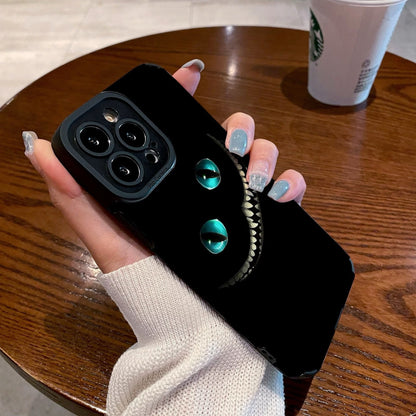 Person holding a black iPhone case with Cheshire Cat of Alice in Wonderland design on a wooden table with a Starbucks cup in the background.