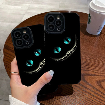 Person holding a black iPhone case with Cheshire Cat of Alice in Wonderland design on a wooden table with a Starbucks cup in the background.