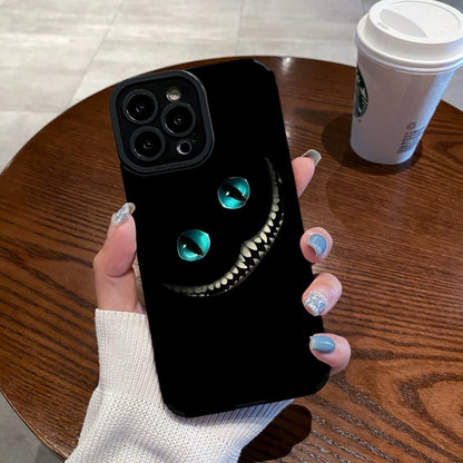 Person holding a black iPhone case with Cheshire Cat of Alice in Wonderland design on a wooden table with a Starbucks cup in the background.