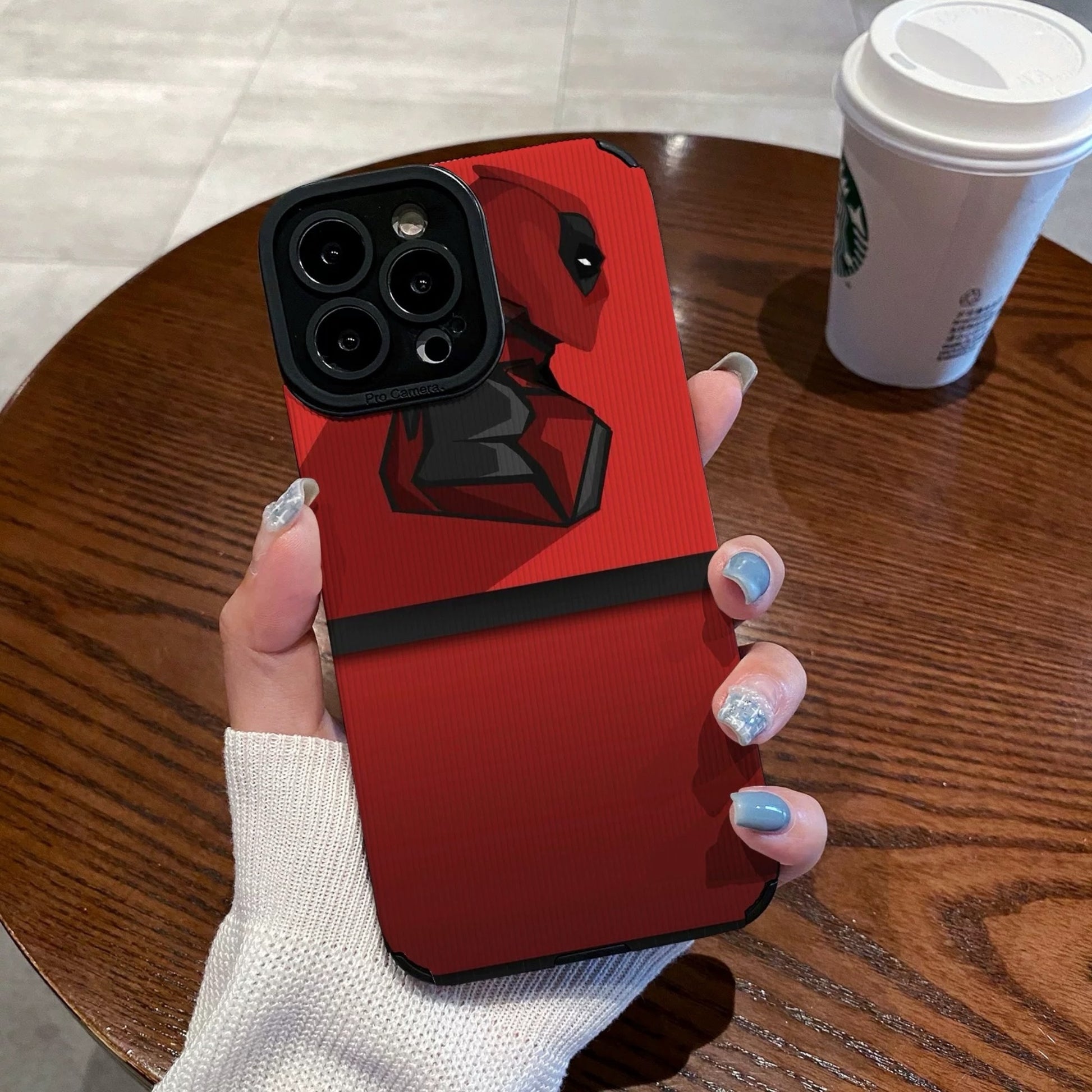 Red iphone case with Dead Pool design held by a hand on a wooden table with a Starbucks cup.