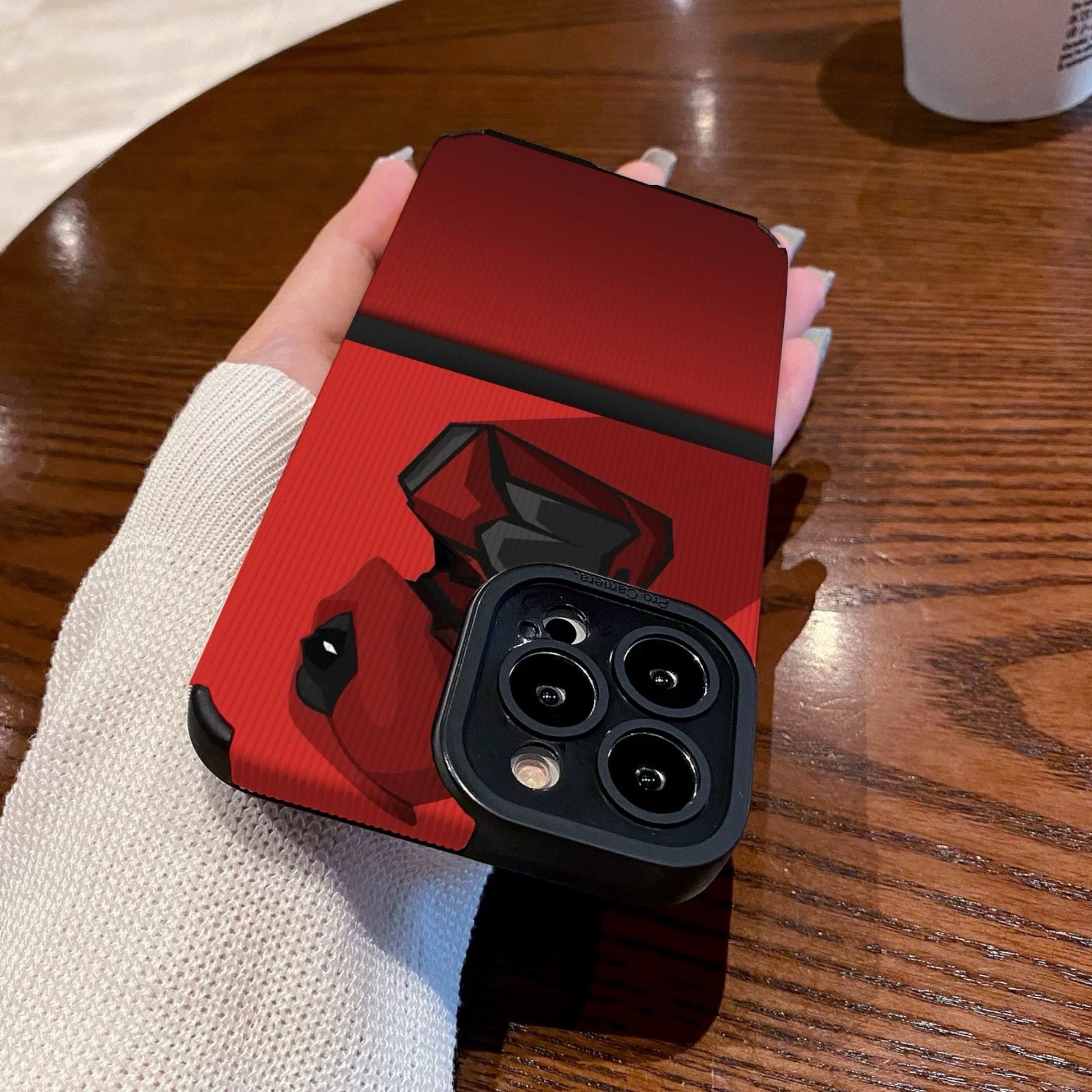 Red iphone case with Dead Pool design held by a hand on a wooden table with a Starbucks cup.