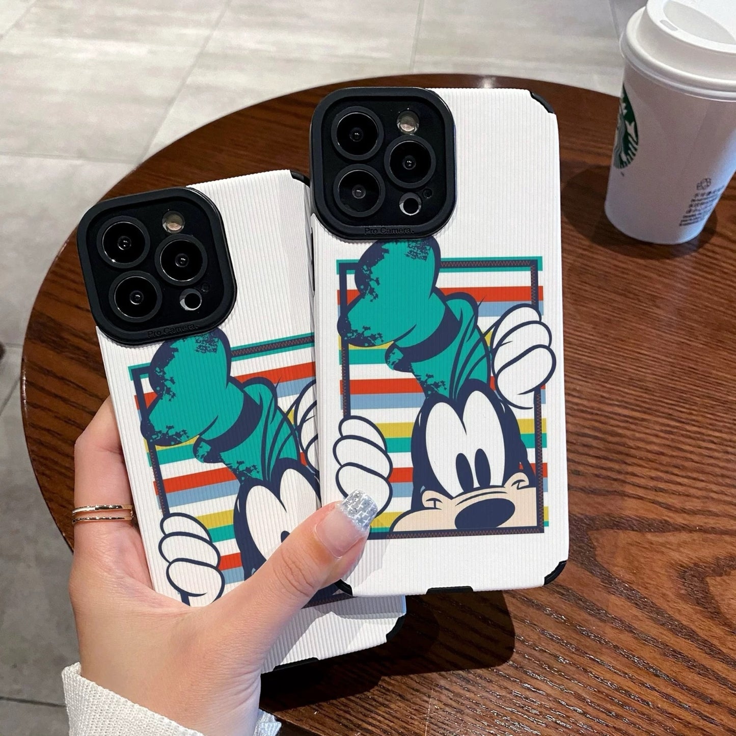 iPhone case with Goofy design held by a person on a wooden table with a Starbucks cup in the background