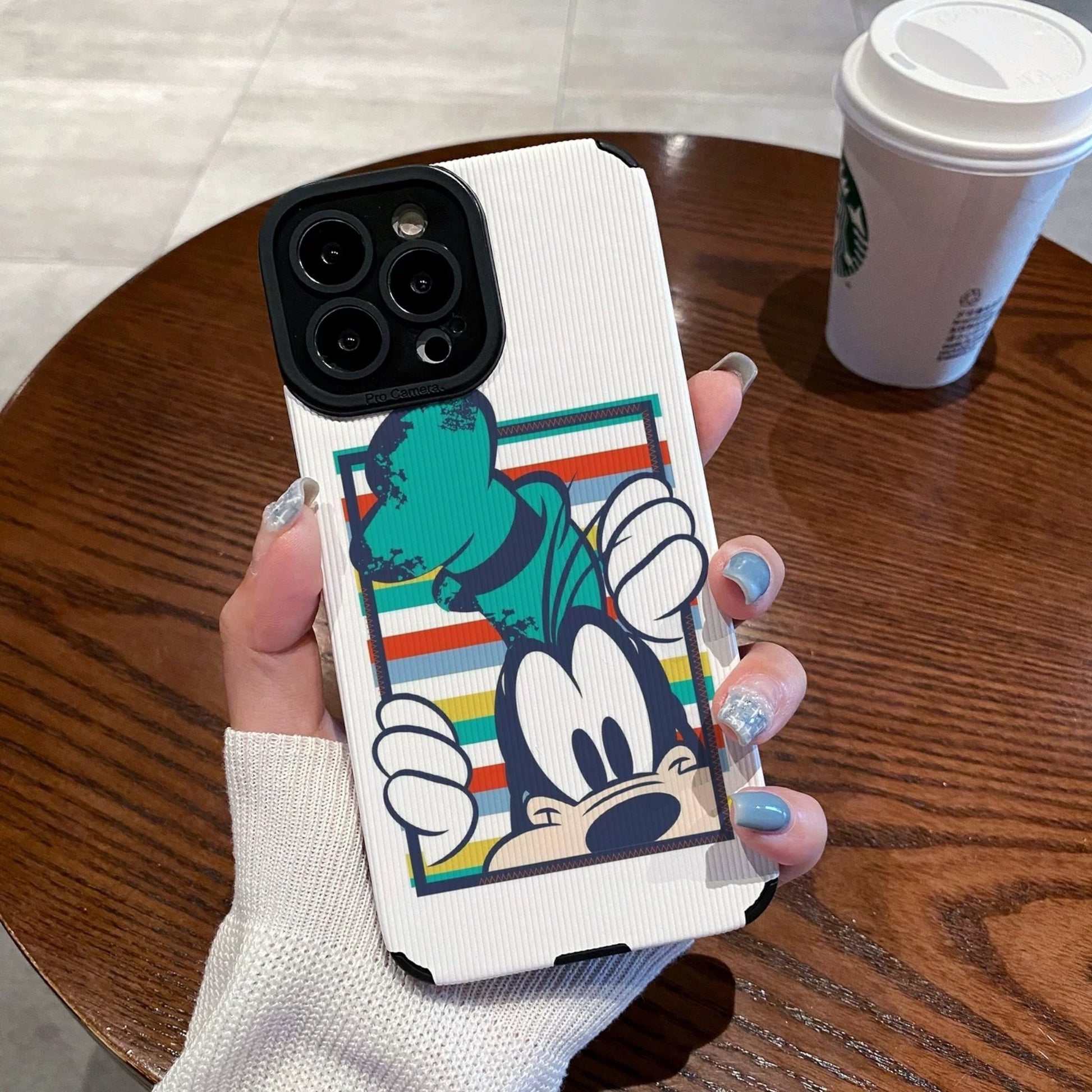 iPhone case with Goofy design held by a person on a wooden table with a Starbucks cup in the background