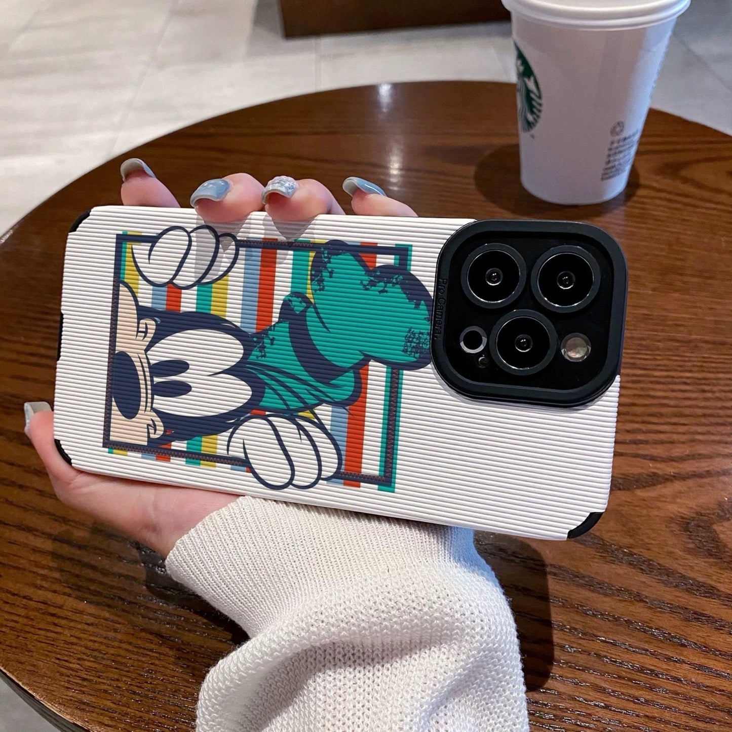 iPhone case with Goofy design held by a person on a wooden table with a Starbucks cup in the background