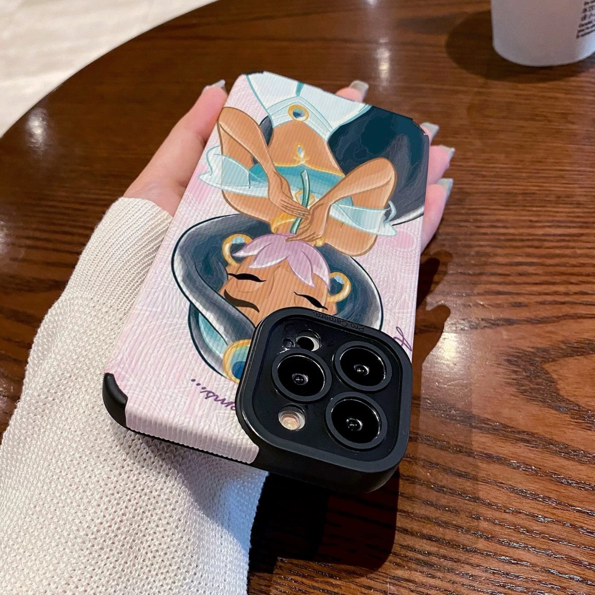 iPhone case with an illustration of a Jasmine holding a flower, held by a hand on a wooden table with a Starbucks cup.