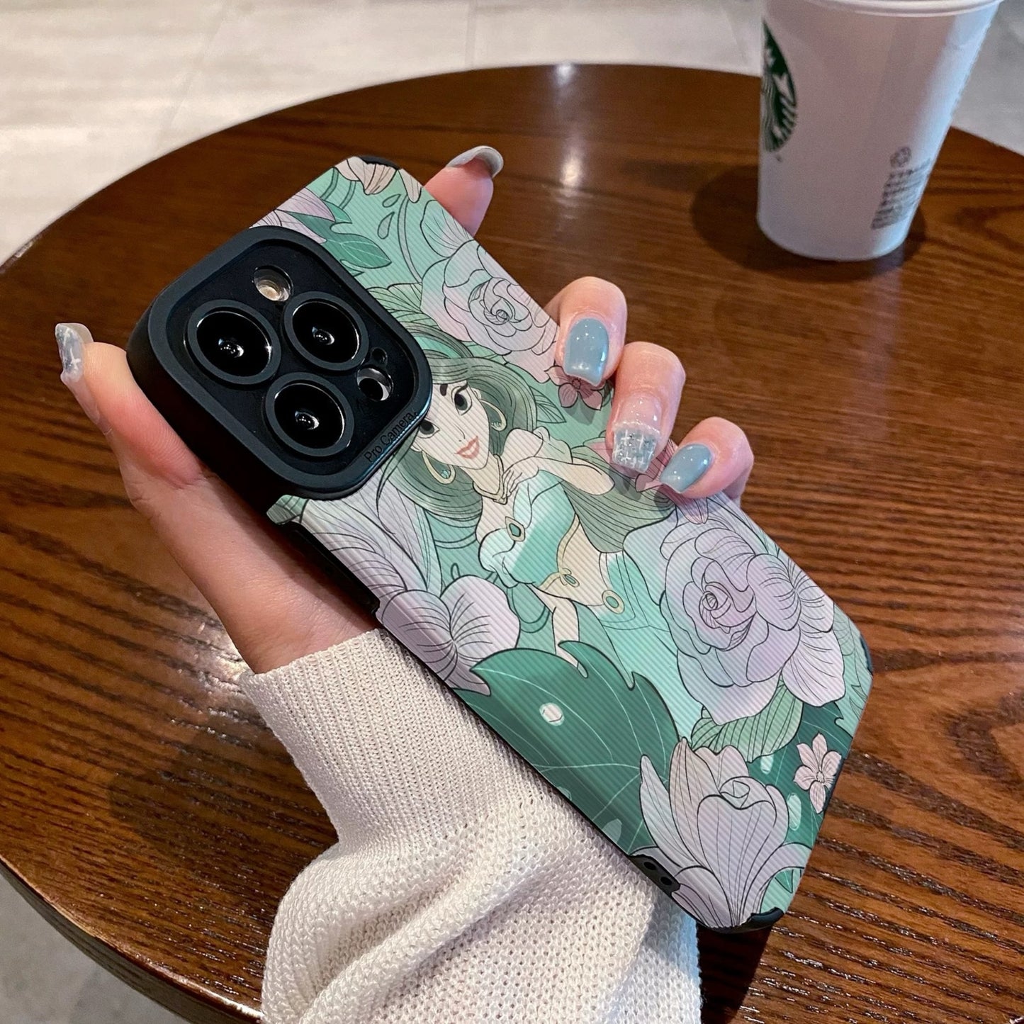 Hand holding a iPhone case with a Jasmine with floral design and character, Starbucks cup in the background.