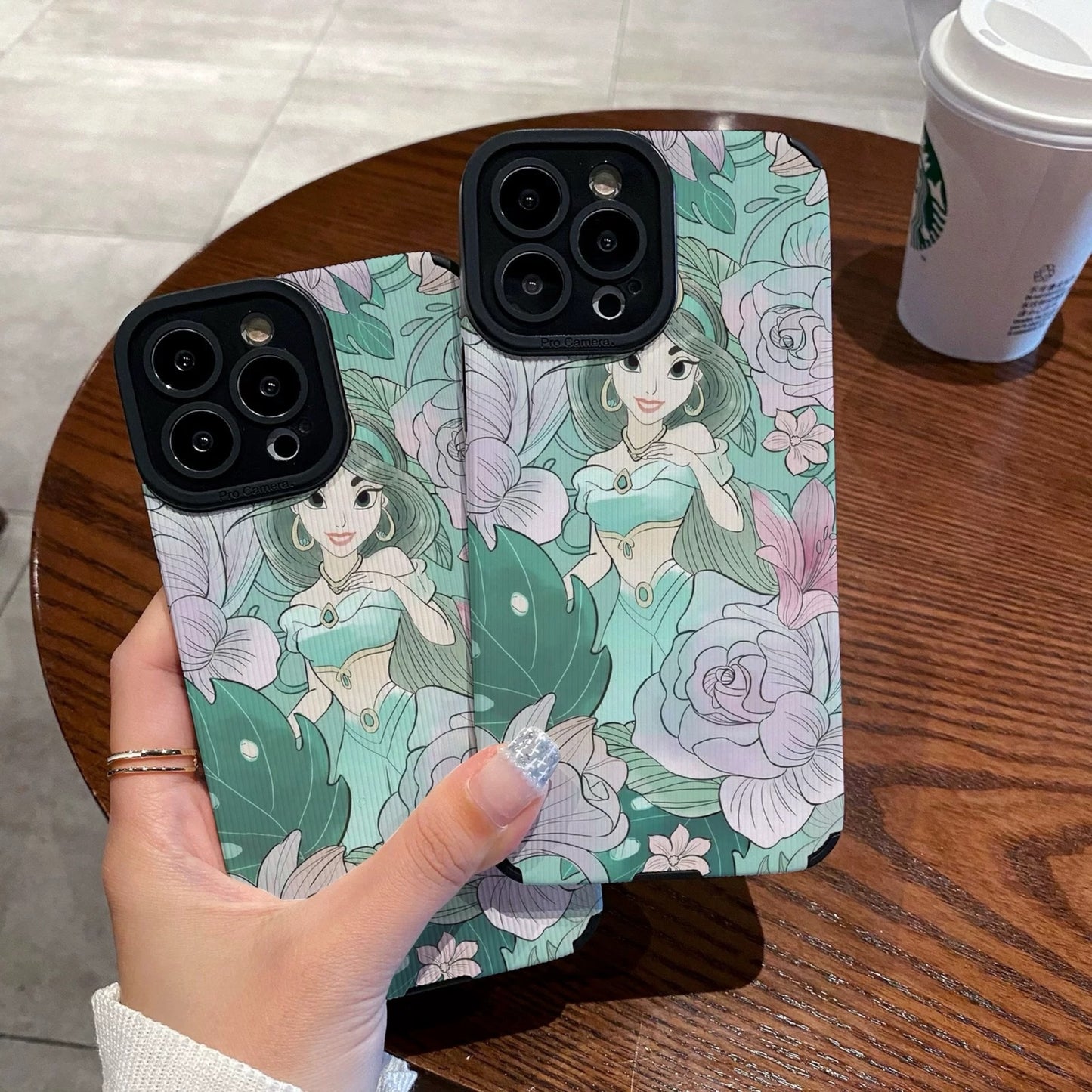 Hand holding a iPhone case with a Jasmine with floral design and character, Starbucks cup in the background.