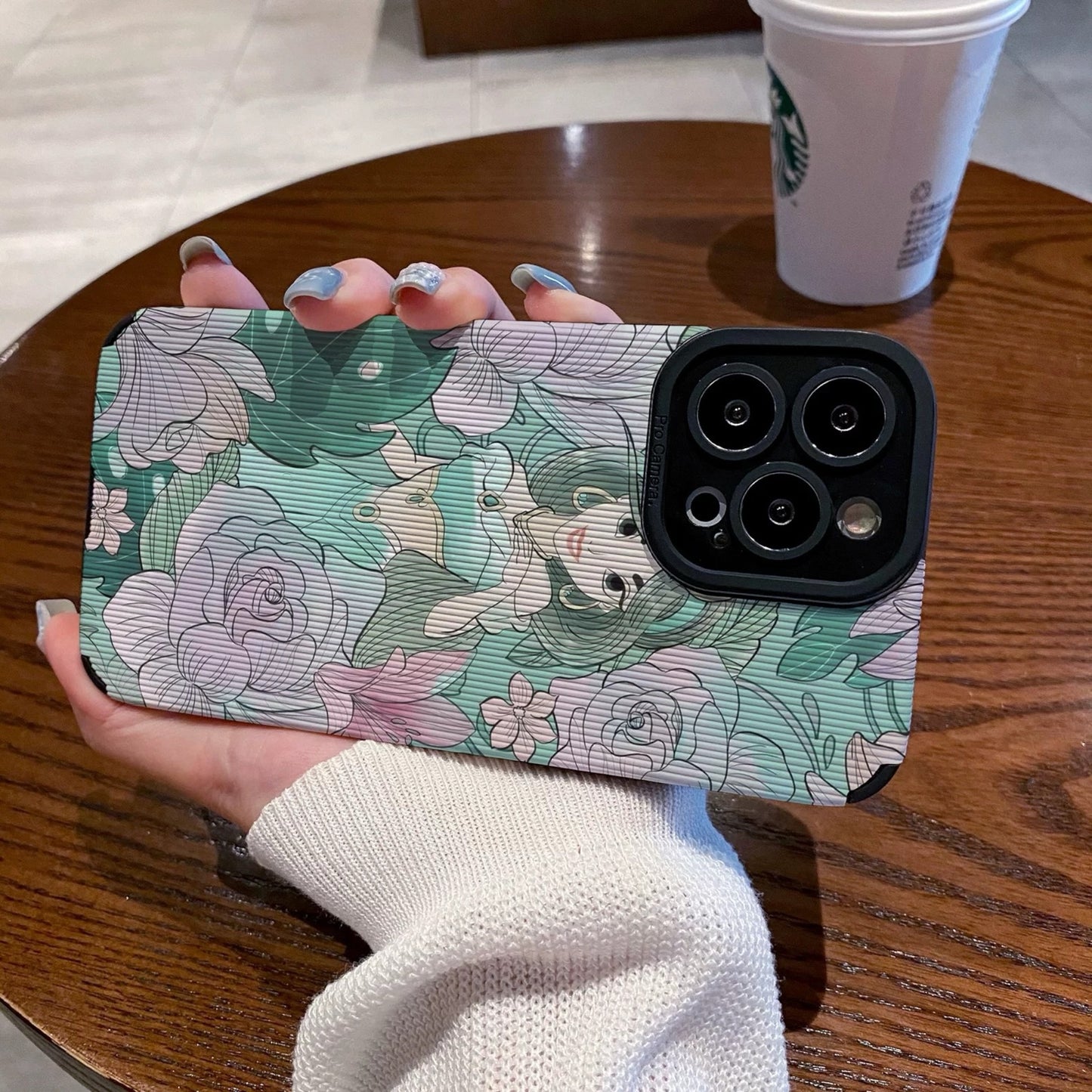 Hand holding a iPhone case with a Jasmine with floral design and character, Starbucks cup in the background.
