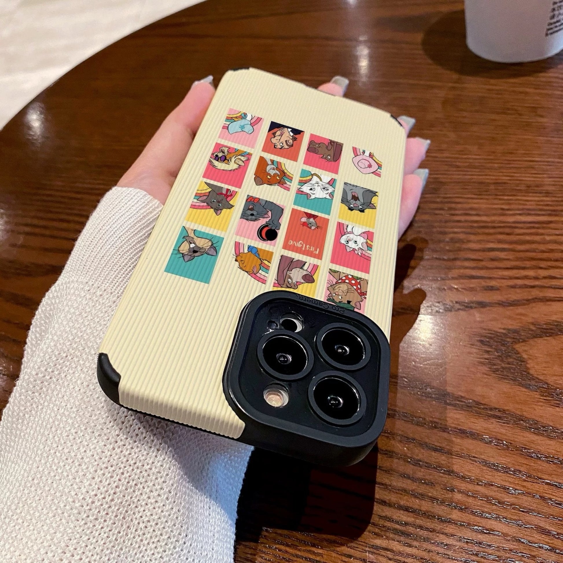 iPhone case with Disney Dogs and Cats character designs held by a person on a wooden table with a Starbucks cup.