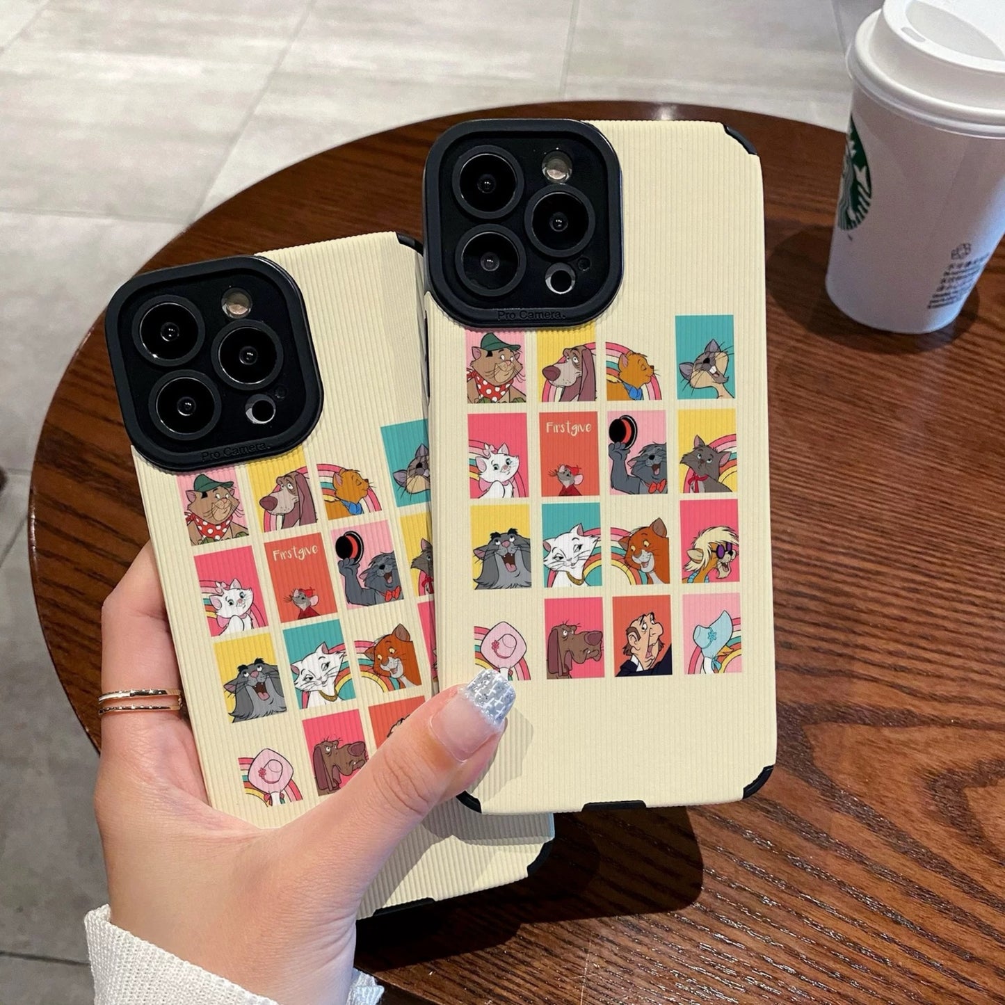 iPhone case with Disney Dogs and Cats character designs held by a person on a wooden table with a Starbucks cup.