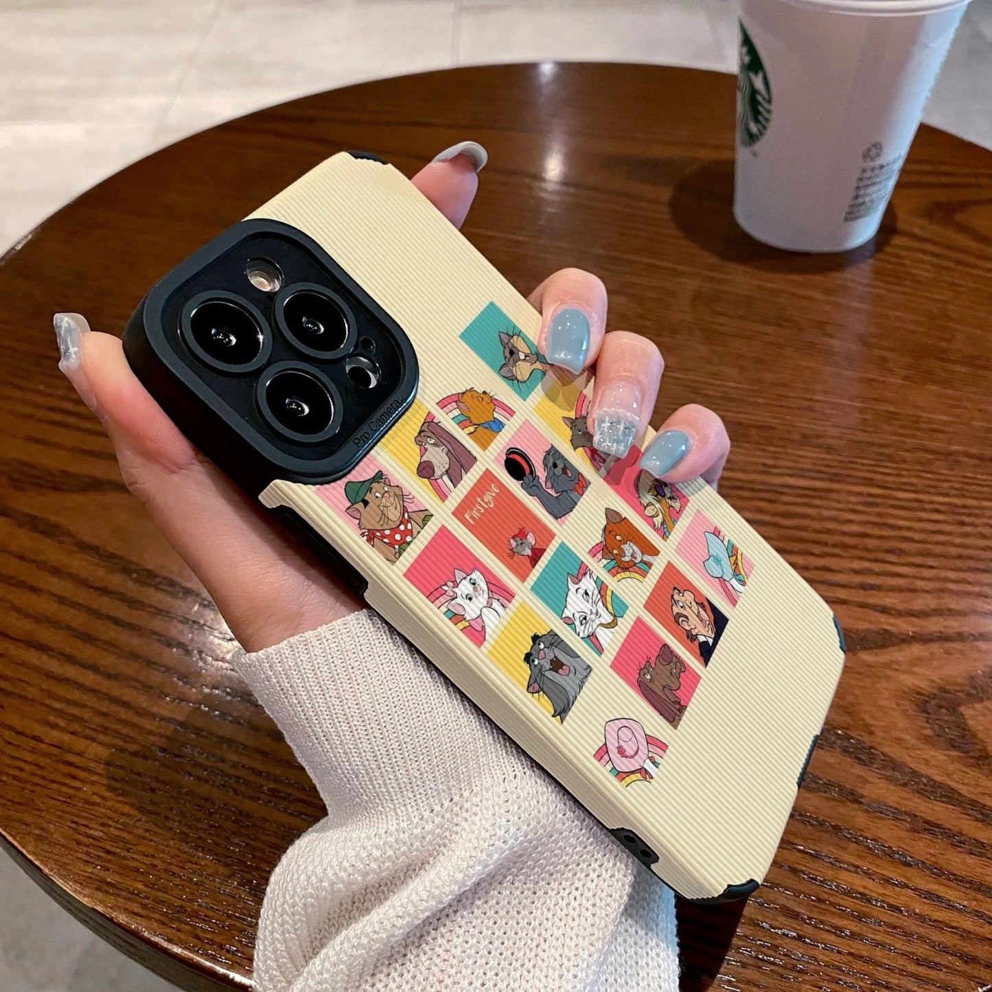 iPhone case with Disney Dogs and Cats character designs held by a person on a wooden table with a Starbucks cup.