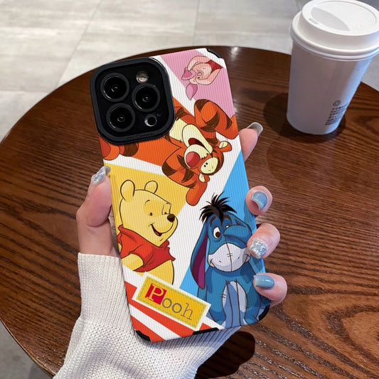Phone case with cartoon characters winnie the pooh and friends held by a hand on a wooden table with a coffee cup.