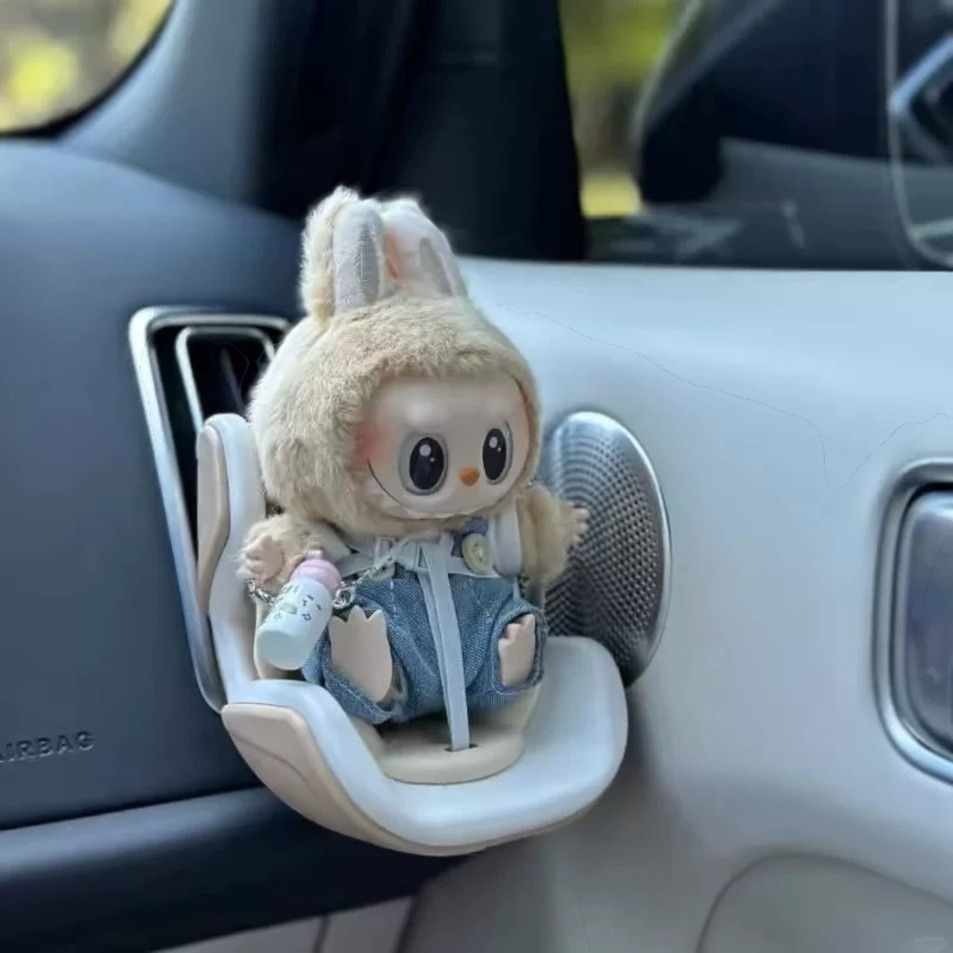 Plush toy Labubu Doll with denim outfit attached to a car's air vent.