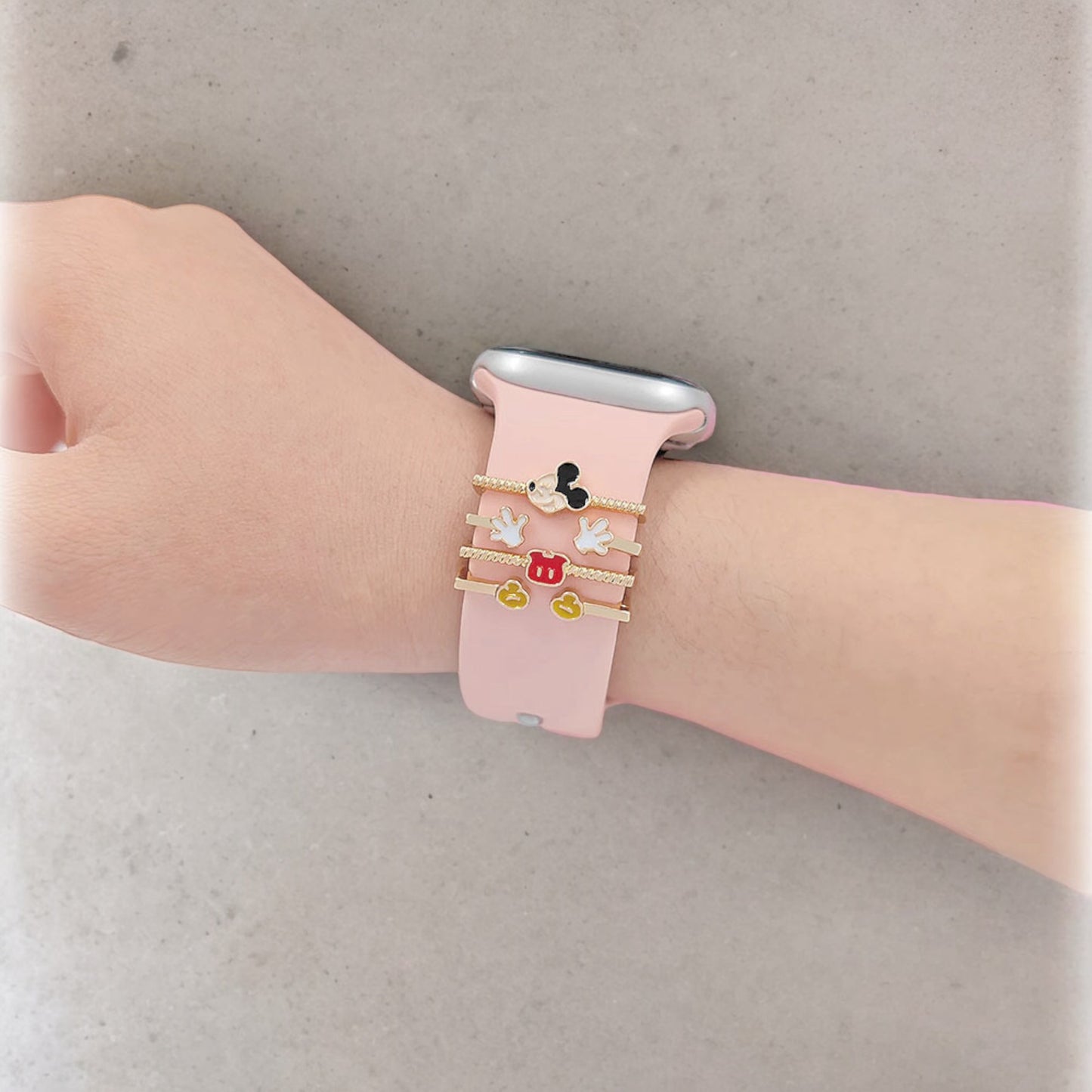 Pink smartwatch with decorative vintage mickey mouse charm on a wrist against a neutral background