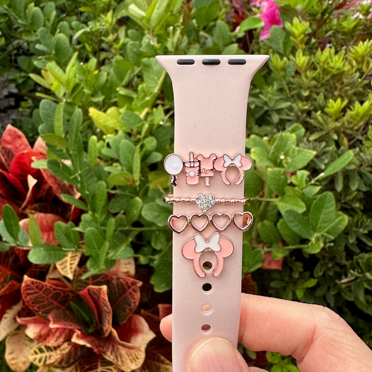 Smartwatch with decorative minnie mouse theme park snack charms held in front of green foliage